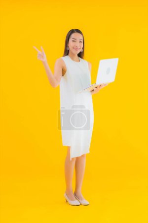 Foto de Retrato hermosa joven asiática mujer con computadora portátil en amarillo aislado fondo - Imagen libre de derechos