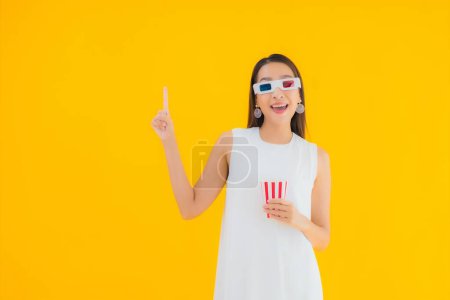 Téléchargez les photos : Portrait belle jeune femme asiatique avec popcorn et lunettes 3D sur fond jaune isolé - en image libre de droit