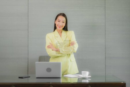 Foto de Retrato hermosa joven mujer asiática uso de ordenador portátil con teléfono móvil inteligente en la mesa de trabajo en la habitación interior - Imagen libre de derechos