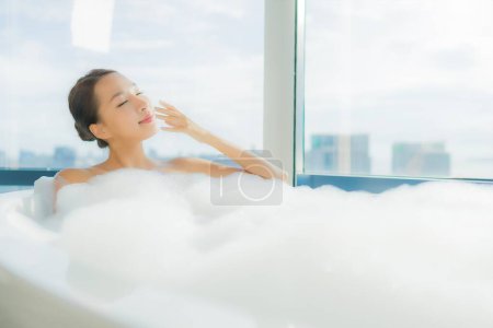 Téléchargez les photos : Portrait belle jeune femme asiatique se détendre profiter dans la baignoire dans la salle de bain intérieure - en image libre de droit