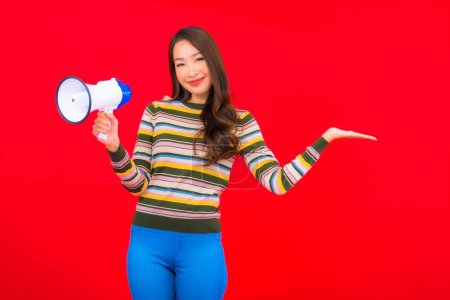 Téléchargez les photos : Portrait belle jeune femme asiatique avec mégaphone pour la communication sur fond rouge - en image libre de droit