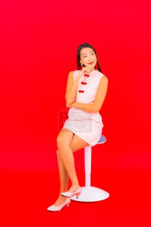 Téléchargez les photos : Portrait belle jeune femme asiatique assis sur chaise sur fond rouge isolé - en image libre de droit