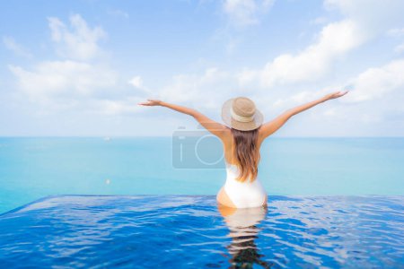 Foto de Retrato hermosa joven mujer asiática relajarse sonrisa ocio alrededor de piscina al aire libre con mar océano en vacaciones de viaje - Imagen libre de derechos