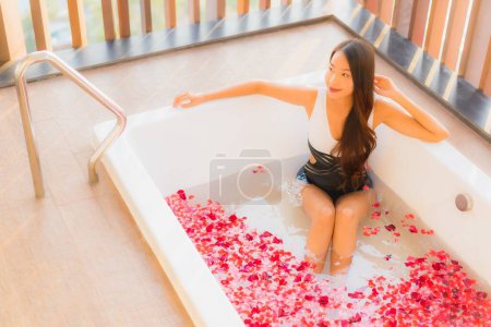Foto de Retrato hermosa joven asiática mujer feliz sonrisa relex en bañera con rosa flor para spa concepto - Imagen libre de derechos