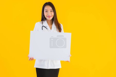Téléchargez les photos : Portrait belle jeune asiatique médecin femme avec tableau blanc vide sur fond jaune isolé - en image libre de droit