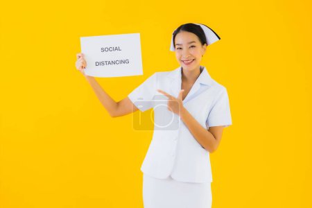 Foto de Retrato hermosa joven asiática mujer tailandesa enfermera mostrar social distanciamiento signo en amarillo aislado fondo - Imagen libre de derechos