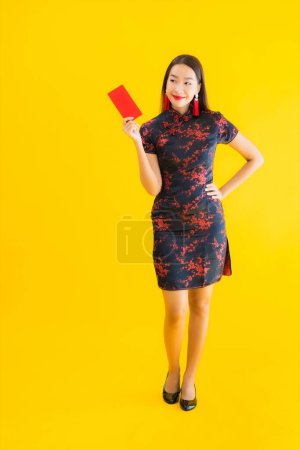 Retrato hermosa mujer asiática joven usar vestido chino con Ang Pao o carta roja con dinero en efectivo para el concepto de año nuevo chino sobre fondo aislado amarillo
