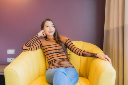 Foto de Retrato hermosa joven asiática mujer relajarse sonrisa en acción en sofá en sala de estar interior - Imagen libre de derechos