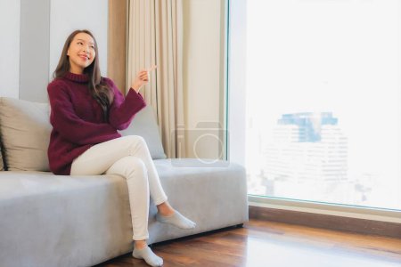 Téléchargez les photos : Portrait belle jeune femme asiatique sourire se détendre sur canapé dans le salon intérieur - en image libre de droit
