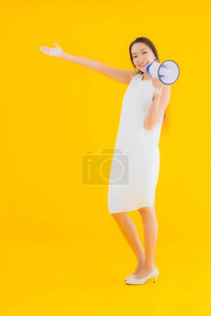 Téléchargez les photos : Portrait belle jeune femme asiatique avec mégaphone sur fond jaune isolé - en image libre de droit