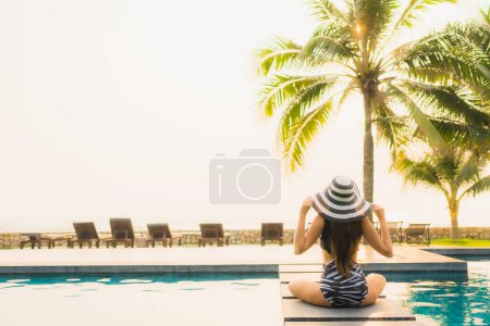 Téléchargez les photos : Portrait belle jeune femme asiatique se détendre autour de la piscine extérieure dans la station hôtelière avec palmier au coucher du soleil ou au lever du soleil pour des vacances de loisirs - en image libre de droit