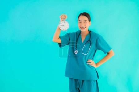 Portriat hermosa joven asiática médico mujer mostrar reloj o alarma en azul aislado fondo
