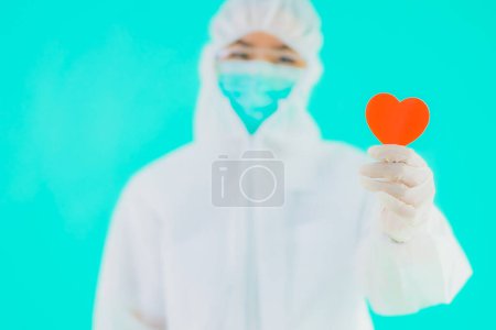 Retrato hermosa joven asiática médico mujer usar ppe o equipo de protección personal para proteger de coronavirus o covid19 mostrar el corazón en azul aislado fondo
