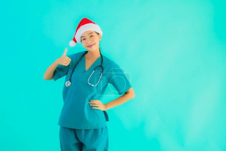 Téléchargez les photos : Portrait belle jeune asiatique médecin femme porter chapeau de Noël avec sourire heureux sur fond bleu isolé - en image libre de droit