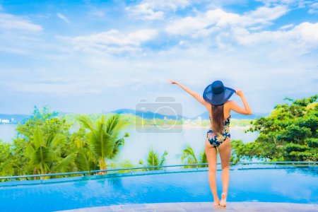 Téléchargez les photos : Portrait belle jeune femme asiatique relax sourire loisirs autour de la piscine extérieure avec vue sur l'océan de mer pour des vacances de voyage - en image libre de droit