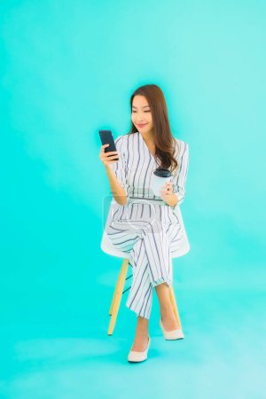 Photo for Portrait beautiful young asian woman use smart mobile phone and sit on chair with blue isolated background - Royalty Free Image