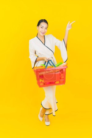 Foto de Retrato hermosa joven negocio asiático mujer con cesta de la compra de comestibles de supermercado sobre fondo amarillo - Imagen libre de derechos