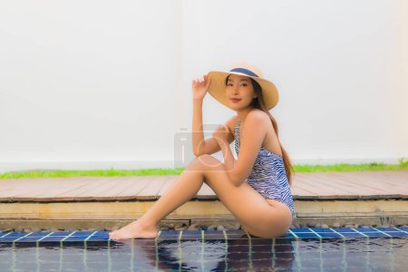 Téléchargez les photos : Portrait jeune femme asiatique sourire heureux se détendre autour de la piscine extérieure dans la station hôtelière pour des vacances de voyage - en image libre de droit