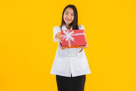 Foto de Retrato hermosa joven asiática médico mujer show rojo regalo caja en amarillo aislado fondo - Imagen libre de derechos