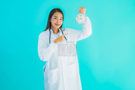 Retrato hermosa joven asiática médico mujer con reloj o alarma en azul aislado fondo
