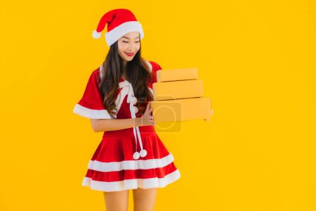 Photo for Portrait beautiful young asian woman wear christmas clothes hat with parcel box packaging ready for shipping on yellow isolated background - Royalty Free Image