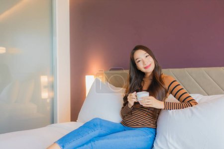 Téléchargez les photos : Portrait belle jeune femme asiatique avec tasse de café sur le lit dans la chambre à coucher intérieur - en image libre de droit
