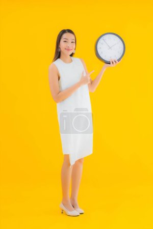 Téléchargez les photos : Portrait belle jeune femme asiatique avec alarme ou horloge sur fond jaune isolé - en image libre de droit