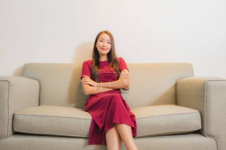 Téléchargez les photos : Portrait belle jeune femme asiatique se détendre sur canapé dans le salon intérieur - en image libre de droit