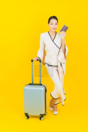 Téléchargez les photos : Portrait belle jeune femme asiatique d'affaires avec sac à bagages et passeport prêt pour le voyage sur fond jaune - en image libre de droit