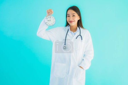 Retrato hermosa joven asiática médico mujer con reloj o alarma en azul aislado fondo
