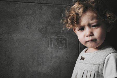 Foto de Retrato de cerca de una linda niña blanca caucásica con una expresión triste en su cara, aislada sobre un fondo oscuro y malhumorado - Imagen libre de derechos