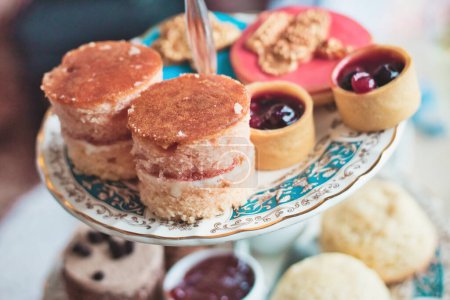 Foto de High tea with ceramic tiered plate stand with scones, cupcakes and mini jam tarts at a kid's birthday party - Imagen libre de derechos