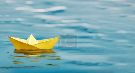 Photo for A single yellow paper boat floating on blue water - symbolic of adventurous future prospects - Royalty Free Image