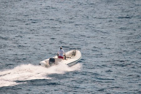 Téléchargez les photos : Photo grand angle d'un homme méconnaissable conduisant un bateau gonflable à coque rigide blanche dans l'eau - en image libre de droit