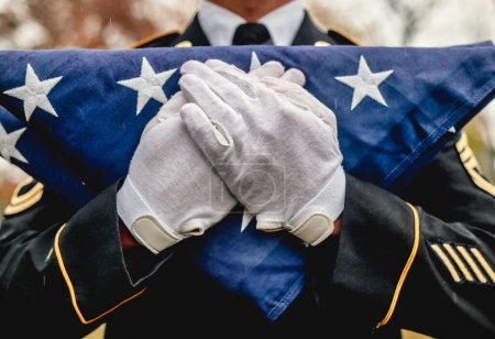 Foto de Primer plano del soldado militar masculino con guantes blancos sosteniendo una bandera estadounidense plegada en una ceremonia conmemorativa - Imagen libre de derechos