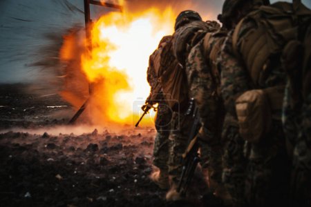 Rear view of a group of US army infantry soldiers on the battleground with an explosion in the background