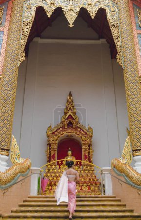 Chica en traje tradicional tailandés que entra en el templo de Wat Phra Singh o Lion Buddha en Chiang Mai