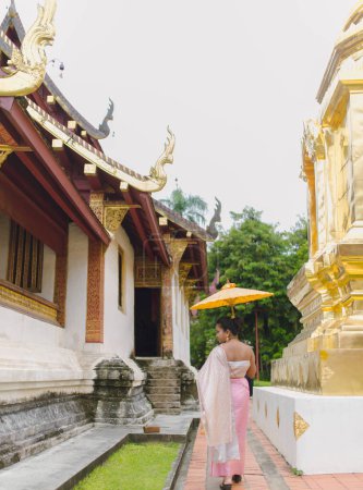 Mujer en traje tailandés mirando hacia atrás cerca de los antiguos templos budistas del norte de Tailandia