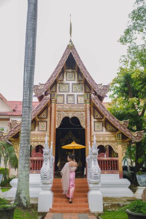 Asiática chica con paraguas entrar en un viejo templo budista en Chiang Mai