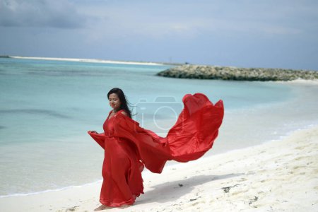 Señora de satén rojo vestido de vuelo que fluye en la playa