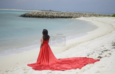 Lady in red satin flying dress flowing at the beach