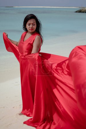 Lady in red satin flying dress flowing at the beach