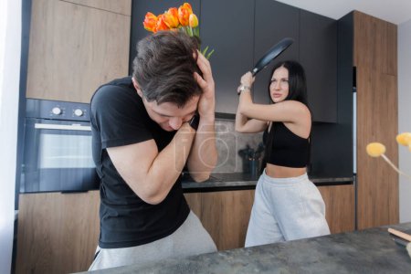 Téléchargez les photos : A man came to his girlfriend with flowers, but she met him with a frying pan. family quarrel.  Infidelity and trust issues. Relationships crisis, conflict. - en image libre de droit