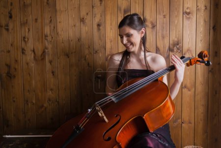 A creative cellist is playing the cello against a wooden background.