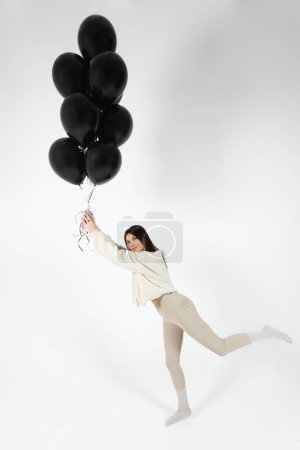 Photo for Brunette Girl in light clothes standing with a Bunch of black balloons and getting lifted up. Isolated on white background. - Royalty Free Image