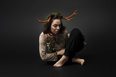 Photo for A portrait of a female druid or shaman with horns, holding ritual talismans in her hands on a black isolated background.Shamanic practices,Spiritual rituals,Pagan beliefs,Nature worship,Mystical. - Royalty Free Image