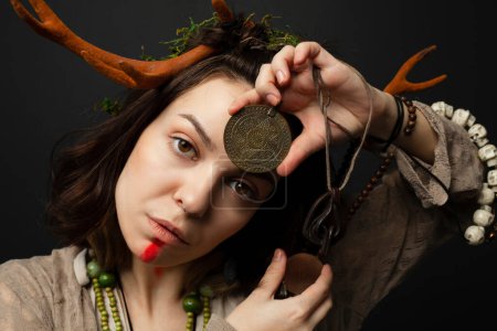 Photo for A portrait of a female druid or shaman with horns, holding ritual talismans in her hands on a black isolated background.Shamanic practices,Spiritual rituals,Pagan beliefs,Nature worship,Mystical. - Royalty Free Image
