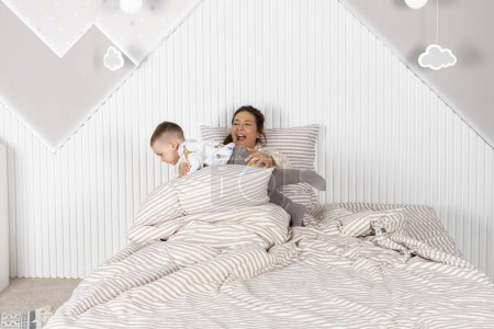 Foto de Una madre y su pequeño hijo están jugando en la cama. - Imagen libre de derechos