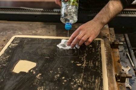 Der Künstler reinigt in einer Kunstwerkstatt einen lithographischen Kalkstein mit einem Klumpen und Chemikalien.