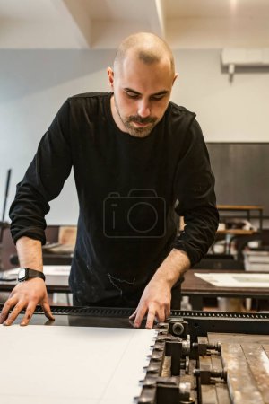 Photo for The artist is placing a paper stencil on a lithographic press or rolling press used for creating lithography in an art workshop. - Royalty Free Image